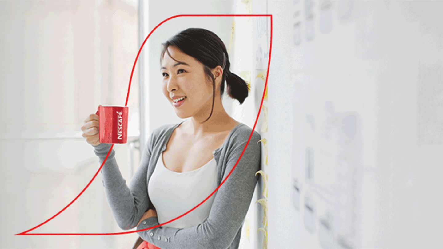 Female leaning back against a wall enjoying a mug of Nescafe coffee